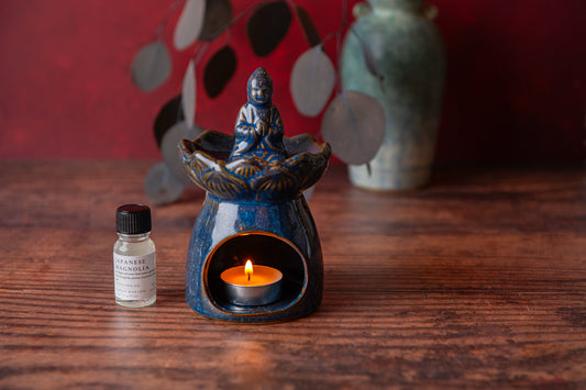 Blue ceramic oil burner with a lit candle and a small bottle on a wooden surface.