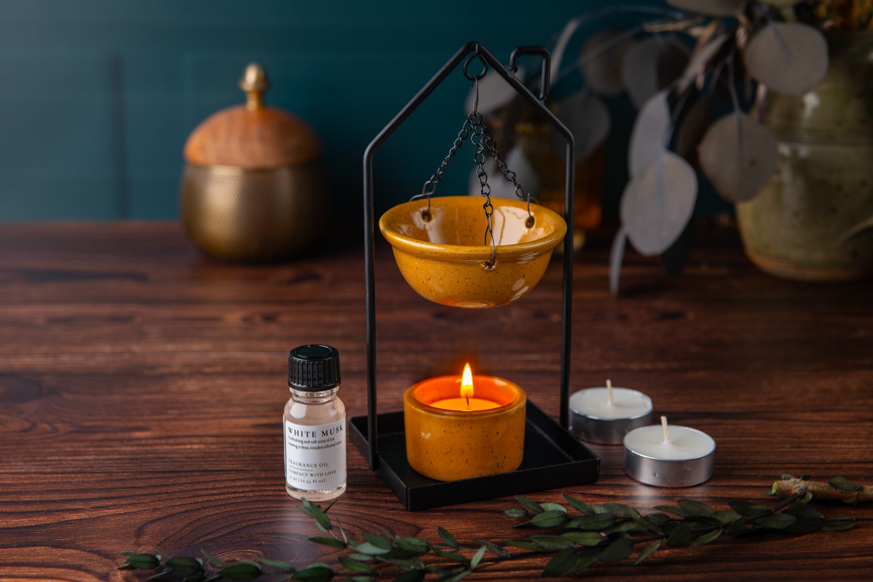 Candle holder with a lit candle and a bottle of essential oil on a wooden surface.