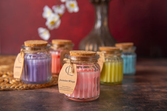 Small jars of colorful candles with visible labels on a wooden surface.