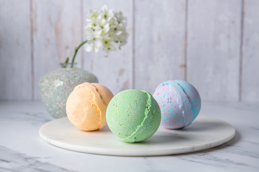 Three colorful bath bombs on a marble tray with a white flower in the background.